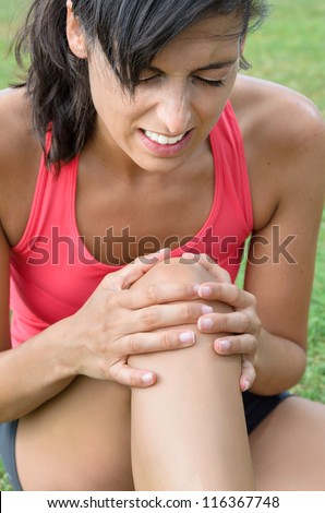 A young woman in pain because of a knee injury. She grabs his knee with his hands with an expression of suffering.