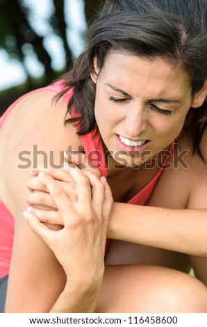 Shoulder injury pain. Sportswoman with painful face expression grabbing her shoulder.