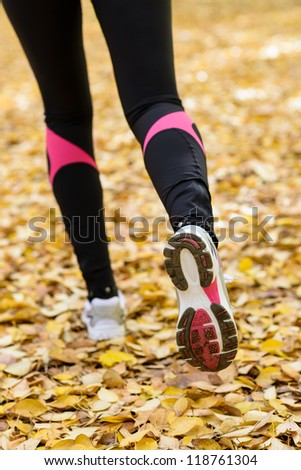 Running exercising concept. Female sportswoman legs running forward with white trainers over a ground full of autumn leaves.