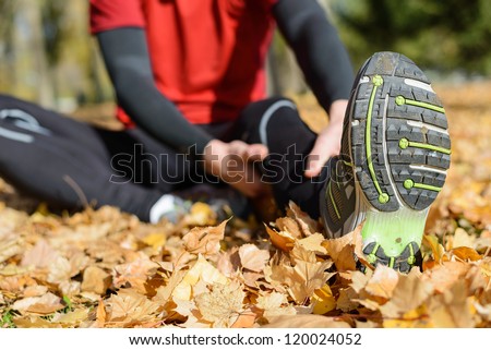 Sportsman stretching painful femoral leg muscle. Sport and injury prevention concept on autumn park outside.
