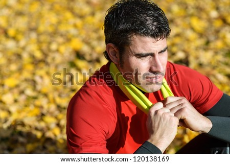 Sportsman tired resting. Sport towel around his neck. Handsome and cheerful athlete sitting and relaxing.