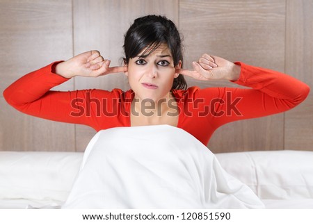 Beautiful brunette caucasian woman covering her ears with her fingers and showing his displeasure. Hispanic model in bed.