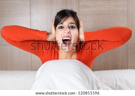 Woman screaming and covering ears on bedroom. Terrifying nightmares. Scared hispanic girl nightmare on bed.