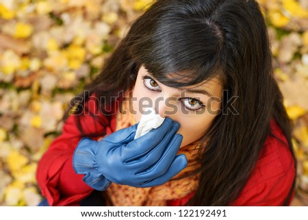 Sad woman sick with the flu or cold blowing the nose with a handkerchief in autumn season. Depressed brunette crying because autumnal illness