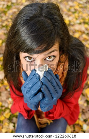 Cute sad woman sick with the flu or cold blowing the nose with a handkerchief in autumn season. Depressed brunette crying because autumnal illness
