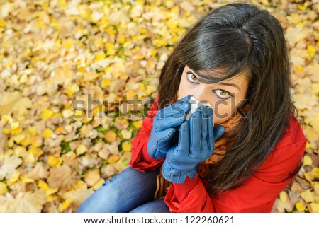 Cute sad woman sick with the flu or cold blowing the nose with a handkerchief in autumn season. Depressed caucasian brunette crying because autumnal illness.