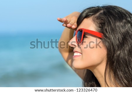 Woman on the beach watching and smiling with blue sea in the background. Caucasian model with red sunglasses looking like life guard.