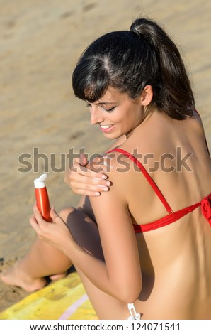 Young woman applying suntan lotion in her shoulder for sunbathing in the beach at summer in a sunny day.