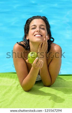 Young woman holding an apple in swimming pool with expression of pleasure. Diet concept on summer with caucasian model.