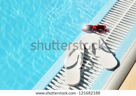 Hot summer concept with white flipflops and red sunglasses at poolside. Sun reflection in glasses.