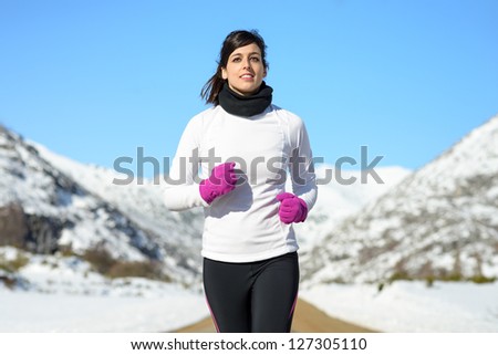 Woman running on winter mountain portrait. Caucasian beautiful female athlete exercising on sunny cold day. Sportswoman with warm sport clothes.