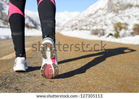 Winter exercising and run concept on mountain road. Female runner shadow and sport footwear.  Copy space