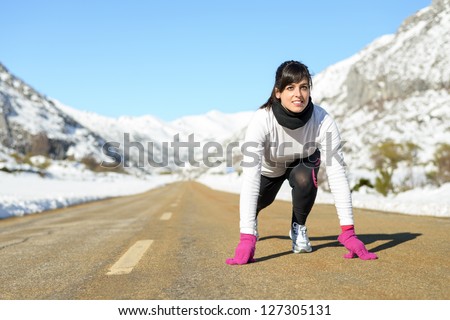 Woman running on winter mountain road. Caucasian female athlete ready to run on snow landscape.