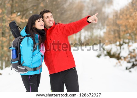 Young happy couple hiking on winter mountain forest. Smiling couple pointing and smiling during walking hike on nature vacations outdoors. Caucasian friends.