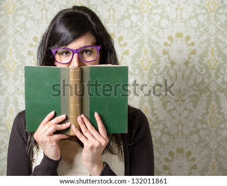Happy woman reading.  Girl looking over old book on retro background. Student smiling behind old book wearing glasses.