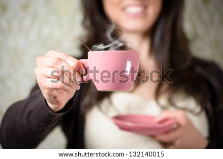 Woman holding hot steaming cup of coffee at home.