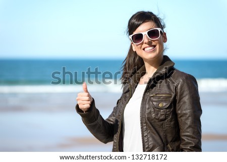 Woman with thumbs up on beach. Positive successful happy girl on sunny spring vacation. Copy space.