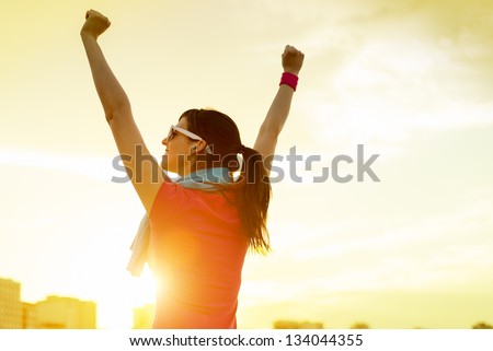 Happy Successful Sportswoman Raising Arms To The Sky On Golden Back Lighting Sunset Summer. Fitness Athlete With Arms Up Celebrating Goals After Sport Exercising And Working Out Outdoors. Copy Space.