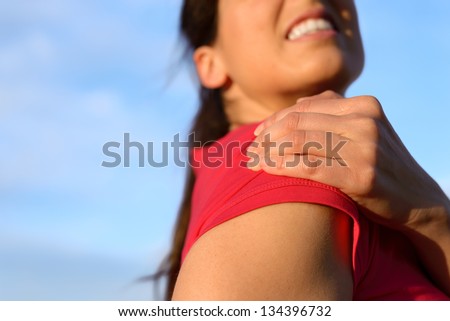 Fitness woman suffering from shoulder injury while exercising. Sky copy space background.
