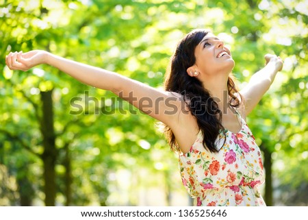 Carefree happy woman in spring or summer forest park raising arms with happiness, hope and vitality. Caucasian girl relaxing and enjoying life on nature outdoors.