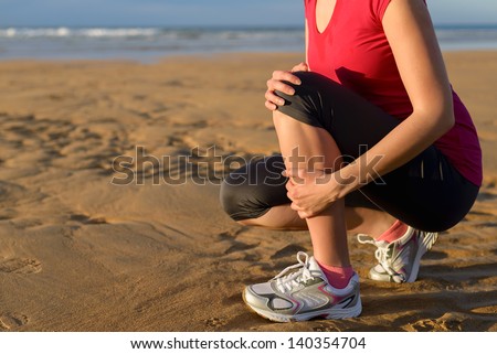 Female runner tibia muscle cramp. Woman clutching her shin because of a running injury and inflammation. Tibial periostitis hurt while jogging on beach.