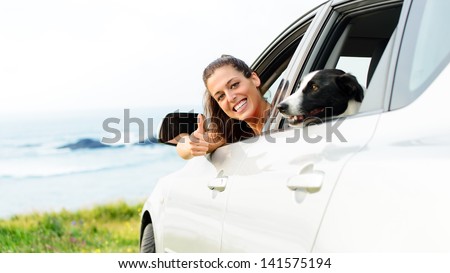 Happy woman traveling in car with dog. Happy woman on road trip with her pet out of the auto window towards coast landscape background.