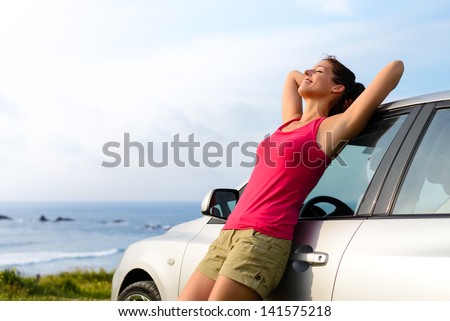 Woman leaning on car on summer travel to coast. Happy girl on road trip enjoying peace and silence relaxing on nature.