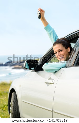 Woman driving car and holding keys on summer travel to coast. Happy female driver out of the auto window.