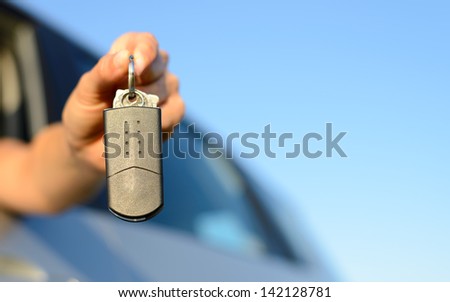 Female hand holding new car keys for rental, buying and travel concept. Copy space blue sky.