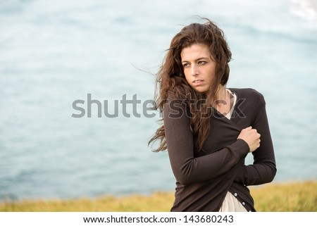 Sad shivery woman in brown sweater jacket hugging herself on late summer cold and windy day on sea background. Sadness, melancholia and heart broken concept.