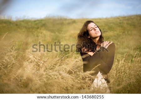 Sad shivery woman in brown sweater jacket hugging herself and walking in nature field on late summer cold day. Sadness, melancholia and heart broken concept.