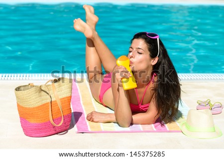 Funny woman sunbathing on summer at swimming pool. Woman enjoying sun with suntan lotion for skin solar protection. Happy playful girl on vacation joking and kissing sunscreen bottle.