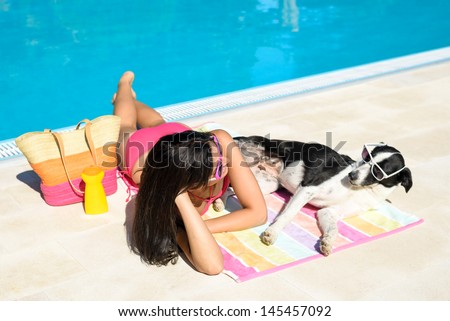Woman and dog sunbathing together on funny summer at swimming pool like if they were talking to each other. Beautiful girl and her pet wearing sunglasses and having fun on holidays at poolside.