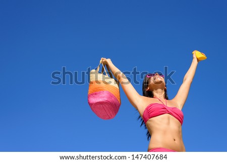 Happy summer vacation. Blissful bikini woman ready for sunbathing protecting skin with sunscreen or suntan lotion. Sexy caucasian girl raising arms to clear blue sky enjoying summertime, heat and sun.