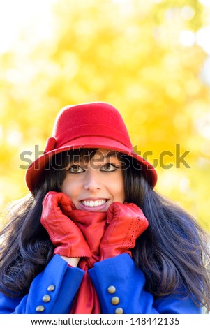 Happy woman in warm clothes shivering on cold autumn day in park. Beautiful female fall portrait on golden nature foliage copy space background.
