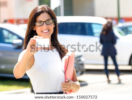 Successful sales business woman in luxury car trade fair. Commercial exhibition and rental vehicle concept. Beautiful female seller showing blank business card.