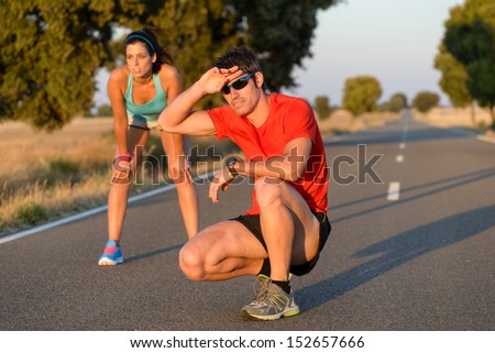Tired fitness couple of runners sweating and taking a rest during marathon training in country road. Sweaty athletes after running hard.