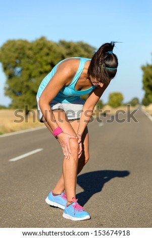Running sport knee injury. Woman runner in pain while training for marathon in country road. Caucasian female athlete.