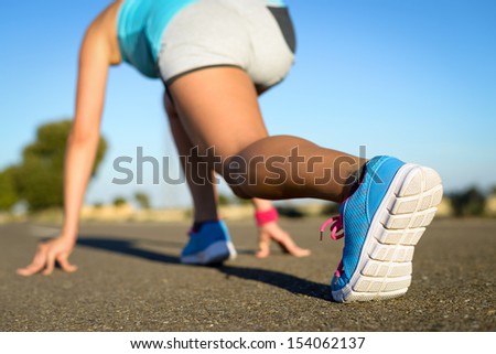 Runner in starting line ready for running and sprint. Sport footwear detail. Female athlete with blue sport shoes training in road.