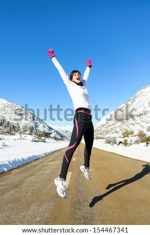 Running and sport success. Happy woman jumping celebrating victory. Female successful runner on winter mountain road.
