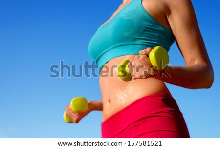 Fitness woman training hard with dumbbells and sweating in summer. Fit sporty girl exercising biceps and arms with weights on blue sky background.