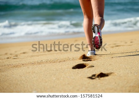 Woman running on beach. Sport footwear, sand footprints and legs close up. Runner feet detail.