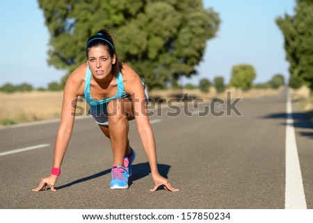 Athletic woman running in countryside road. Fitness female runner in ready start line pose outdoors in summer sprint challenge.