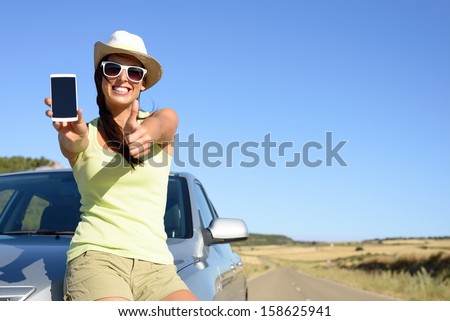 Young woman leaning on car showing cell phone screen and doing thumbs up gesture. Positive woman giving her approval to car insurance service.