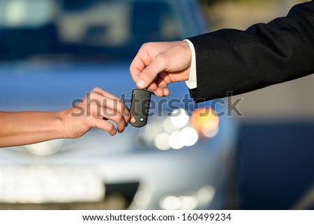 Car salesman giving key to female buyer. Vehicle sales or rental concept.
