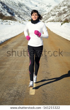 Woman Running In Winter. Girl Exercising On A Mountain Road On A Snowy Natural Scenery.