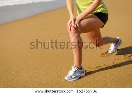 Fitness girl warming up and stretching before running in beach. Woman with running knee injury.