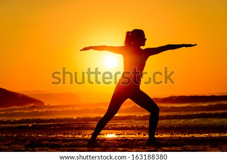Yoga exercises in beach on beautiful summer sunset alone. Fit female silhouette relaxing, breathing and exercising.