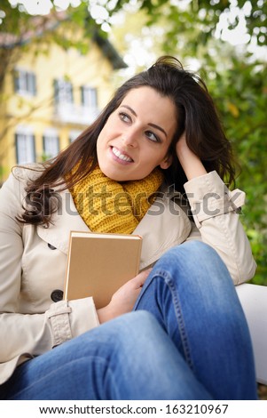 Woman reading book and day dreaming at home garden. Female enjoying relaxing lecture and tranquility in front of country house.