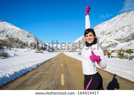 Woman celebrating success and achievement after running in cold winter mountain road. Female runner raising arm and doing thumbs up approving gesture.